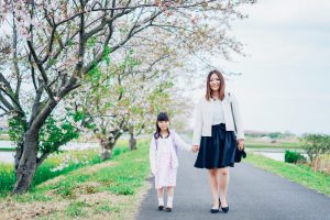 春の写真。母親と娘が桜の道を歩いている。
